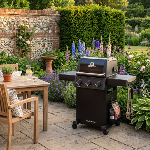 Mid Ulster Garden Centre Broil King Crown 310 Shadow matte black gas BBQ on a patio in a lush garden setting.