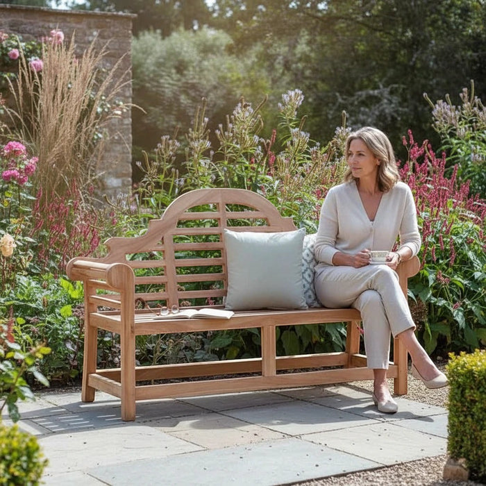 Mid Ulster Garden Centre Bramblecrest Lutyens style teak garden bench with a woman sitting in a lush garden.